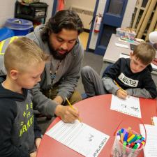 Male Indigenous Support Worker sit with two elementary student boys, working on an assignment