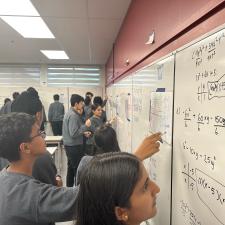 Group of students writing math equations on a white board